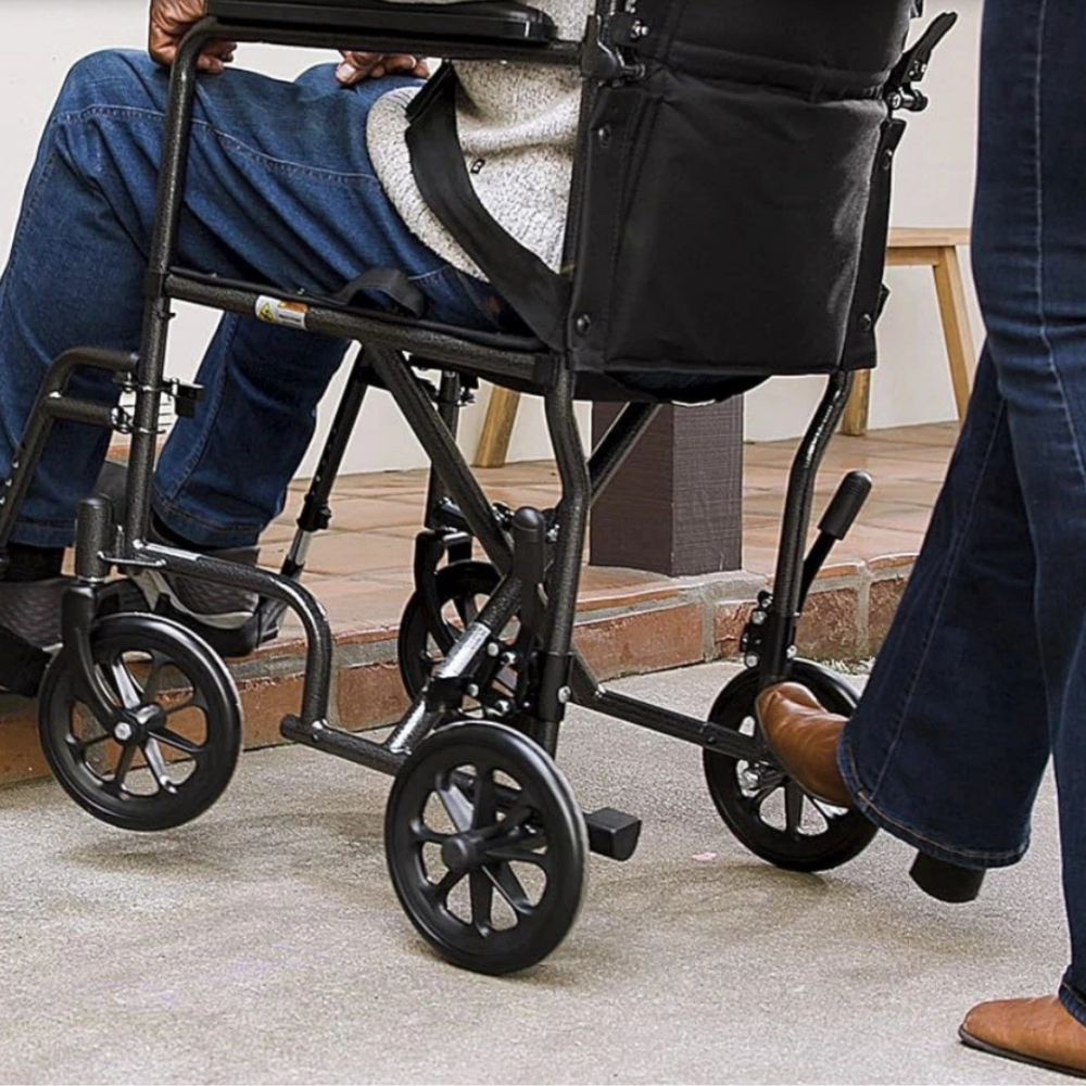 Close-up lifestyle image showing a caregiver pushing the Drive Medical transport chair along a paved outdoor path.