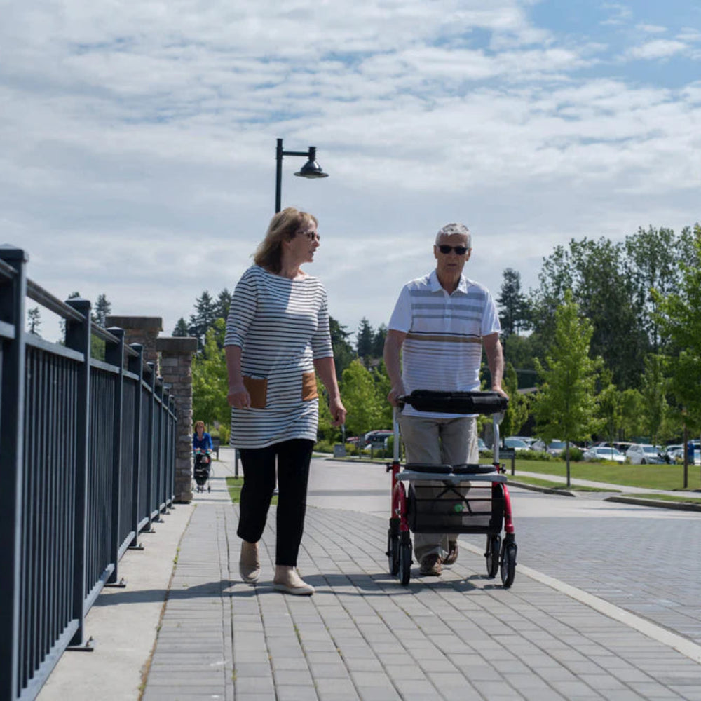 Two individuals walking across a sunny outdoor bridge, navigating smoothly with their lightweight Evolution Xpresso Lite CF rollators.