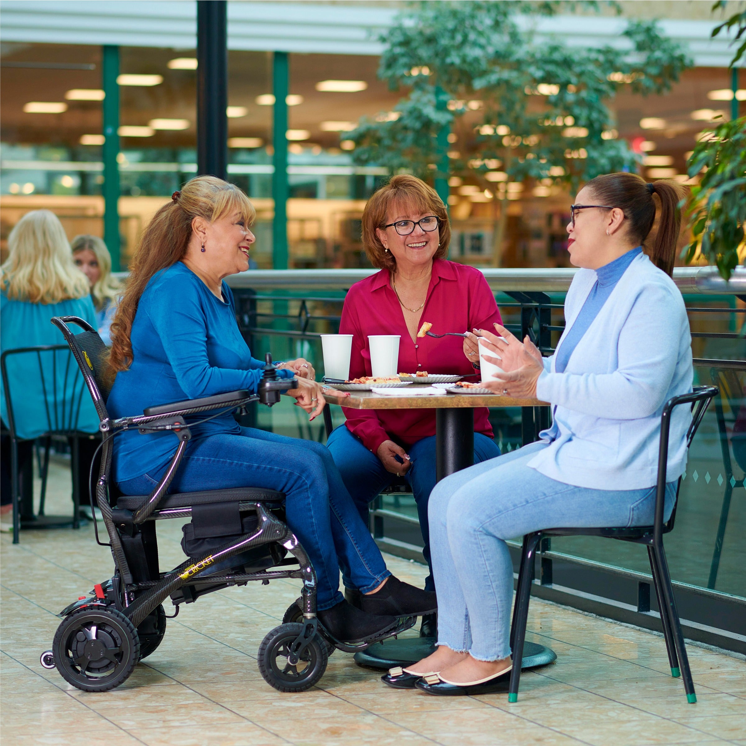 Woman in a Golden Cricket GP302 power wheelchair chatting with two friends at a café table
