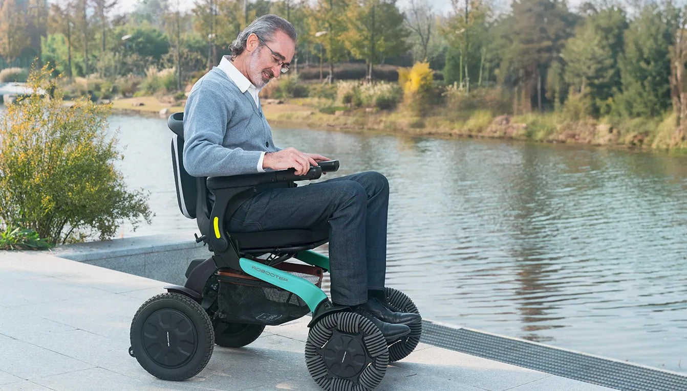 Lifestyle shot of a user navigating grassy, uneven terrain near a lake using the rugged Robooter E60 all-terrain power wheelchair.