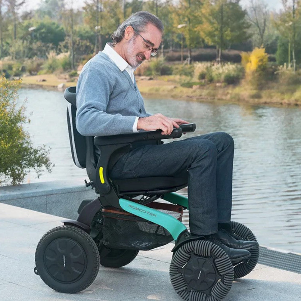Lifestyle shot of a user navigating grassy, uneven terrain near a lake using the rugged Robooter E60 all-terrain power wheelchair.