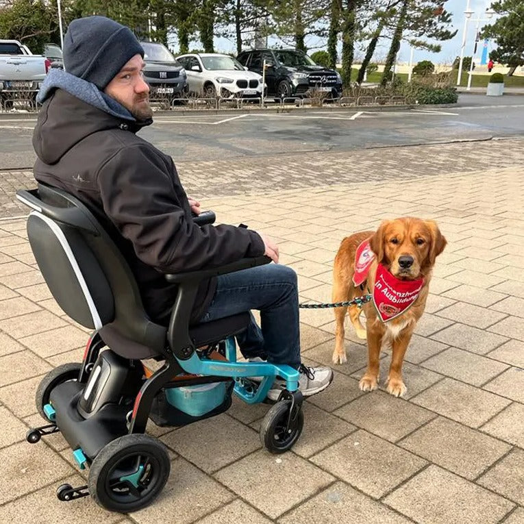 Man and his dog outdoors, seated in a teal Robooter E40 power wheelchair