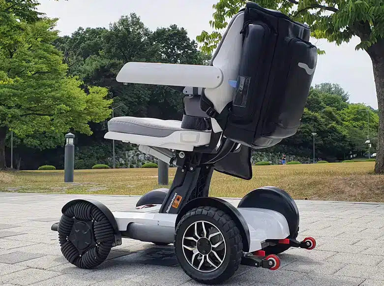 Side profile lifestyle image of the black Robooter X40 power chair outdoors, featuring the precision-mounted custom storage backpack.