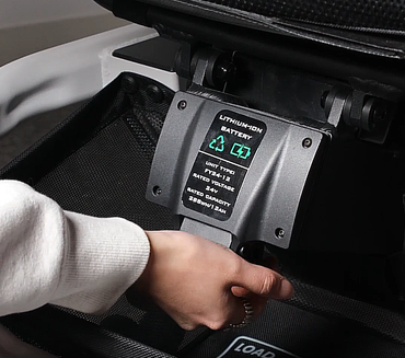 Person seamlessly sliding the high-capacity 24V lithium-ion replacement battery into the Travel Buggy GT power wheelchair.