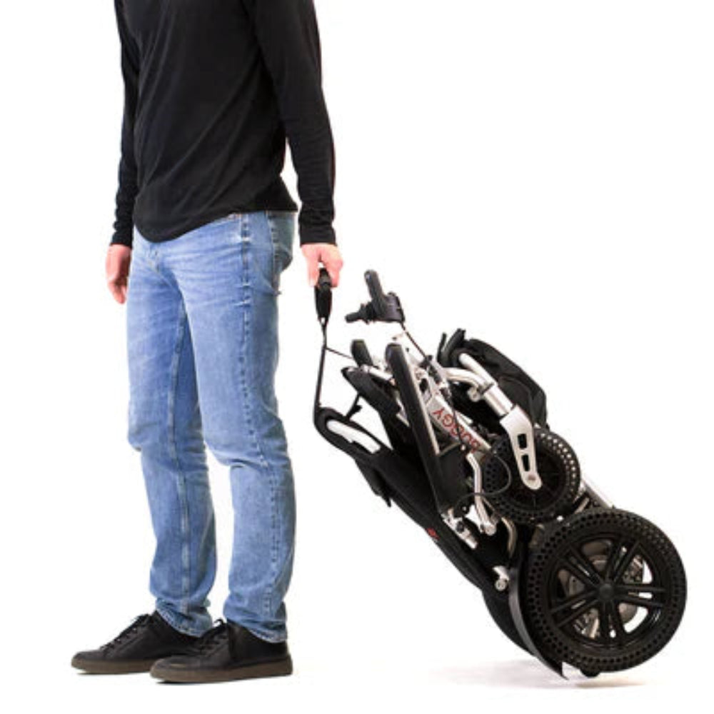 Person effortlessly pulling a folded Travel Buggy electric wheelchair like a suitcase using the innovative Easy-Lift strap.