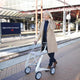 Woman walking through a train station with an Oyster White byACRE Carbon Ultralight rollator