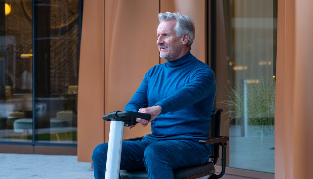Man riding a white WHILL Model R scooter outside a modern building