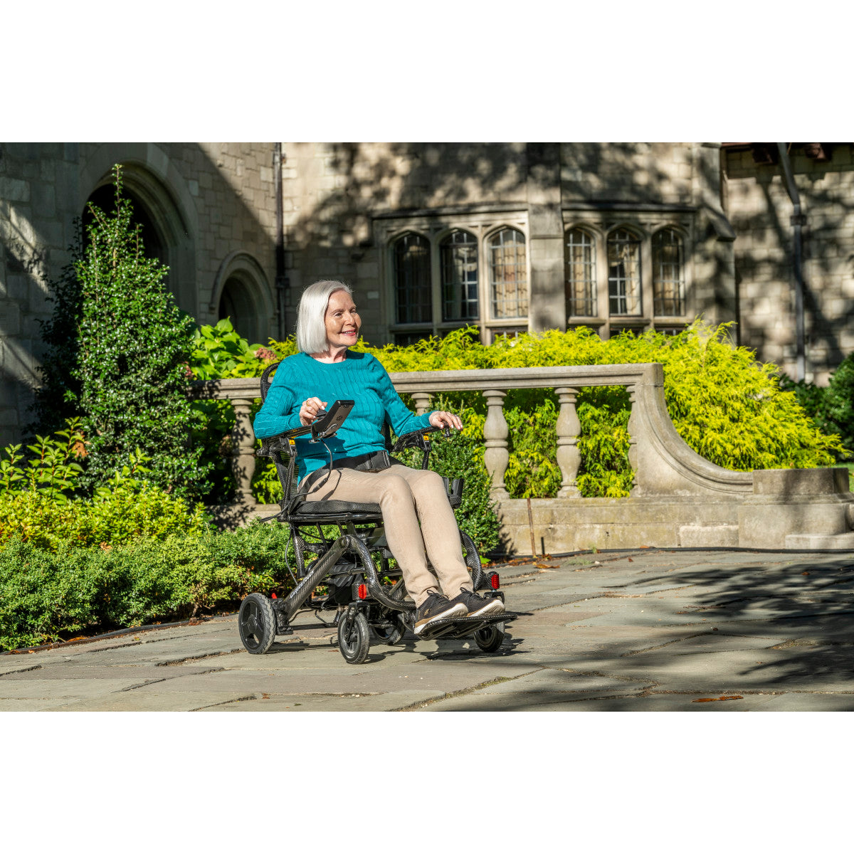Woman driving a Drive Medical CarbonTouch power wheelchair in a garden courtyard