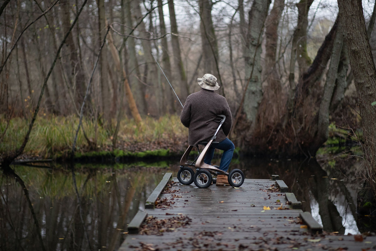 Person seated on a Bentley Brown byACRE Carbon Overland rollator while fishing outdoors