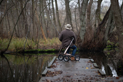 Person seated on a Bentley Brown byACRE Carbon Overland rollator while fishing outdoors