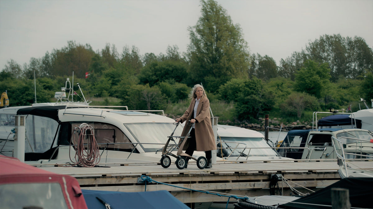 Person using a Bentley Brown byACRE Carbon Overland rollator along a marina dock