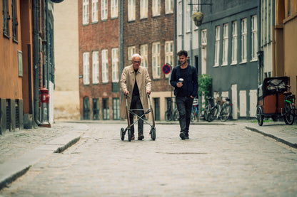 Person using a Bentley Brown byACRE Carbon Overland rollator on a cobblestone street