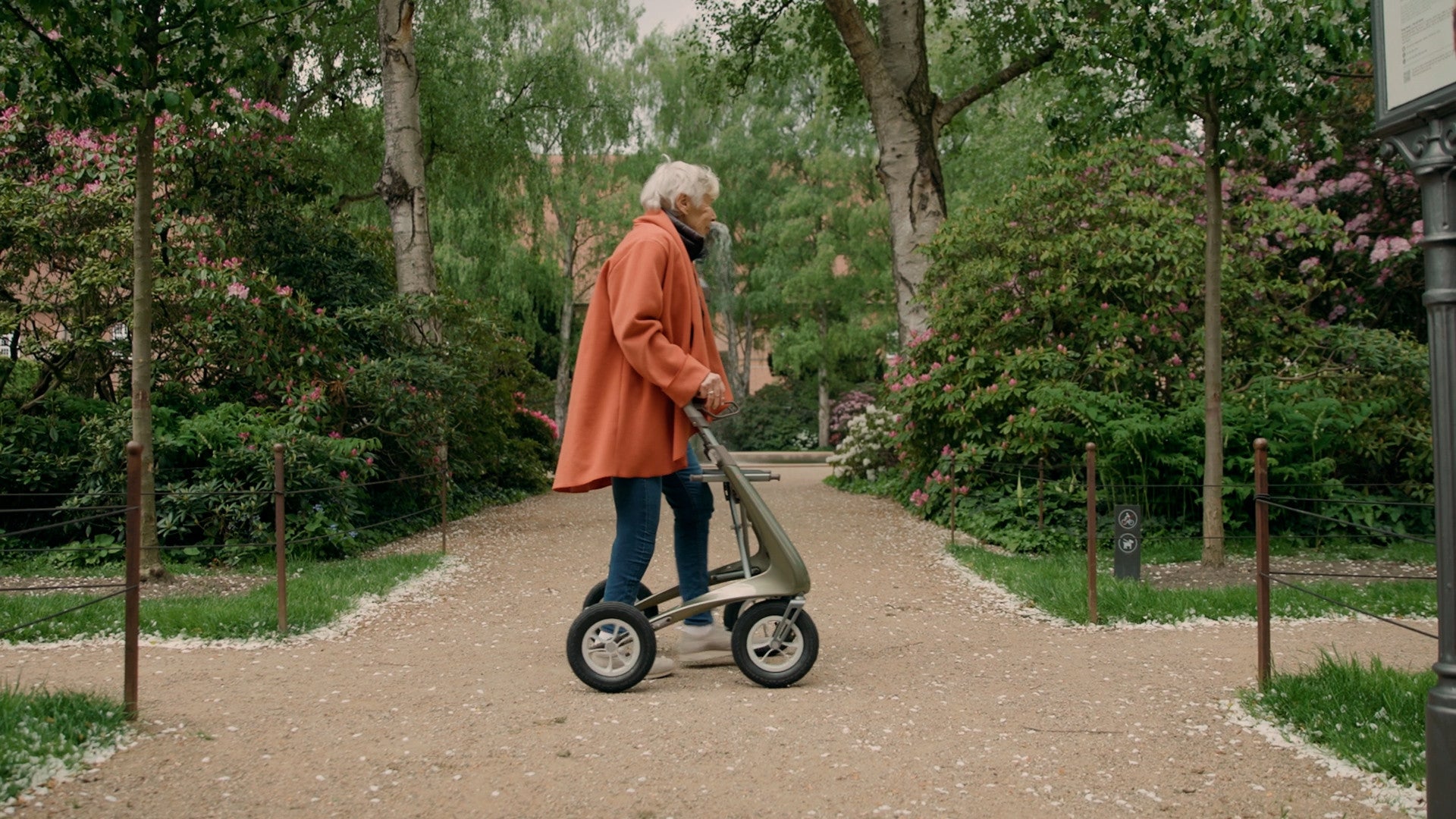 Woman walking a park path with a Defender Green byACRE Carbon Overland rollator