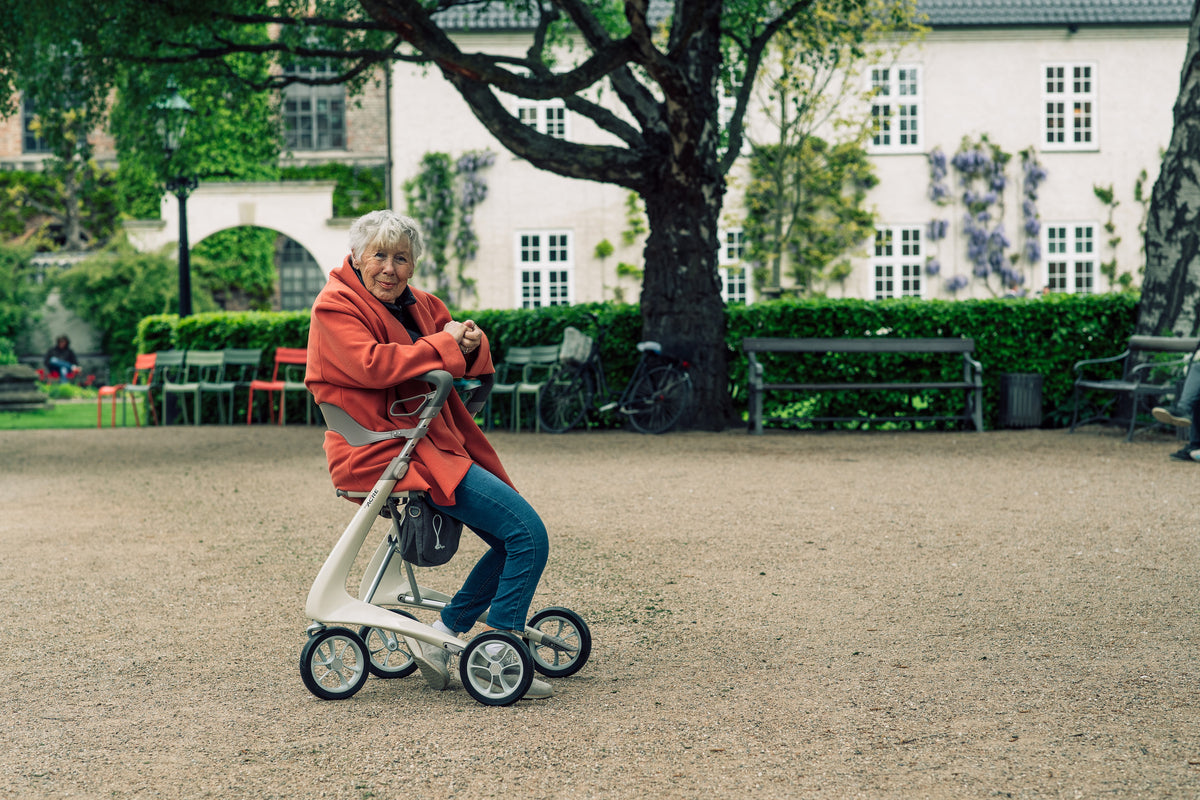 Woman sitting on the seat of an Oyster White byACRE Carbon Ultralight rollator in a city park