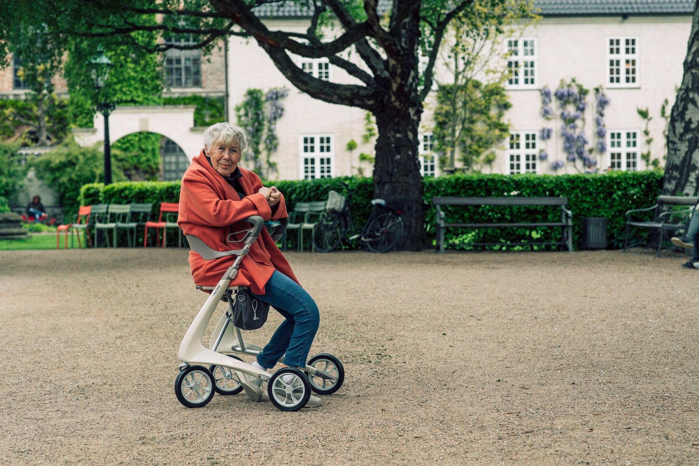 Woman sitting on the seat of an Oyster White byACRE Carbon Ultralight rollator in a city park