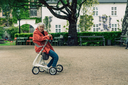 Woman sitting on the seat of an Oyster White byACRE Carbon Ultralight rollator in a city park
