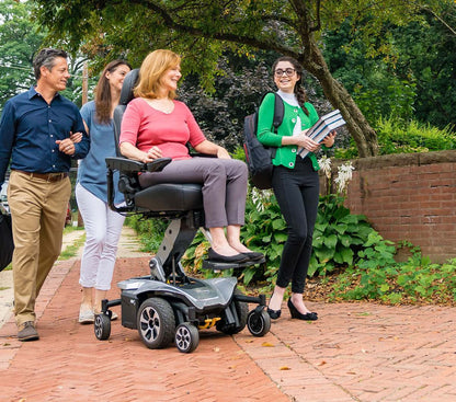 Woman using a Jazzy Air 2 power wheelchair with companions on a paved path