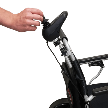 Caregiver's hand comfortably steering the power wheelchair using the Travel Buggy rear-mounted joystick bracket.