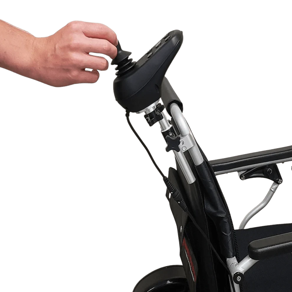 Caregiver's hand comfortably steering the power wheelchair using the Travel Buggy rear-mounted joystick bracket.