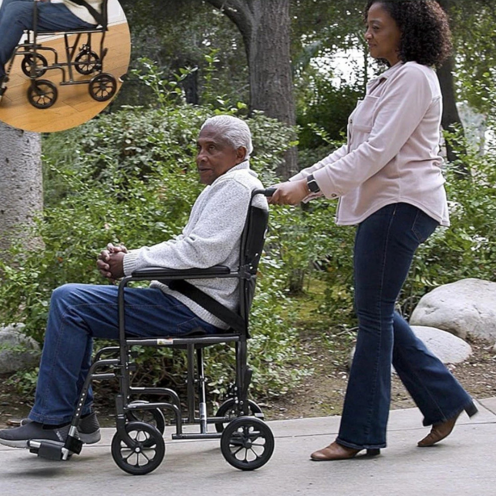 Lifestyle shot of a woman pushing a man in the Drive Medical Steel Transport Chair through a scenic, sunny park setting.