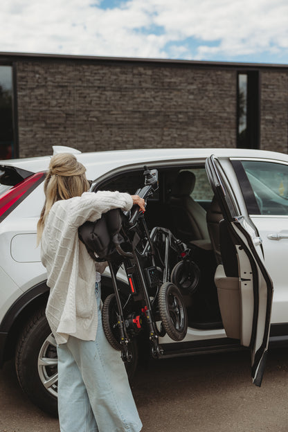 Person loading a folded Travel Buggy AEROLUX 2C power wheelchair into a car