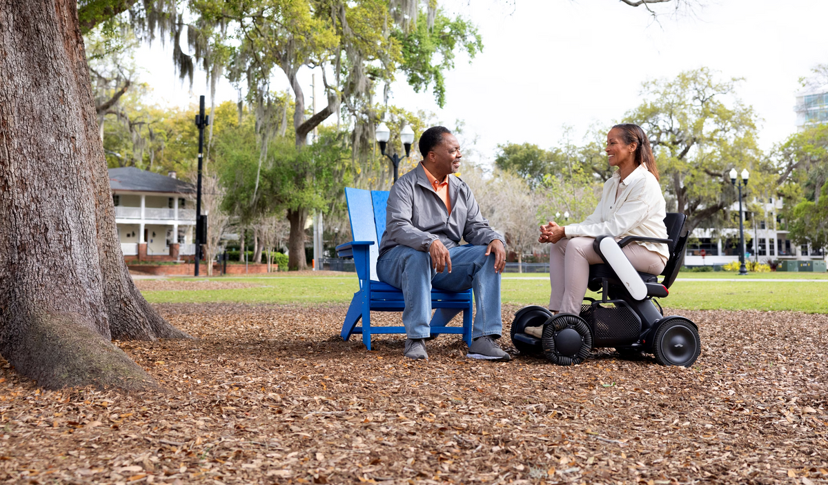 Woman using a WHILL Model C2 power wheelchair beside another person in a park