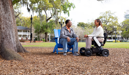 Woman using a WHILL Model C2 power wheelchair beside another person in a park