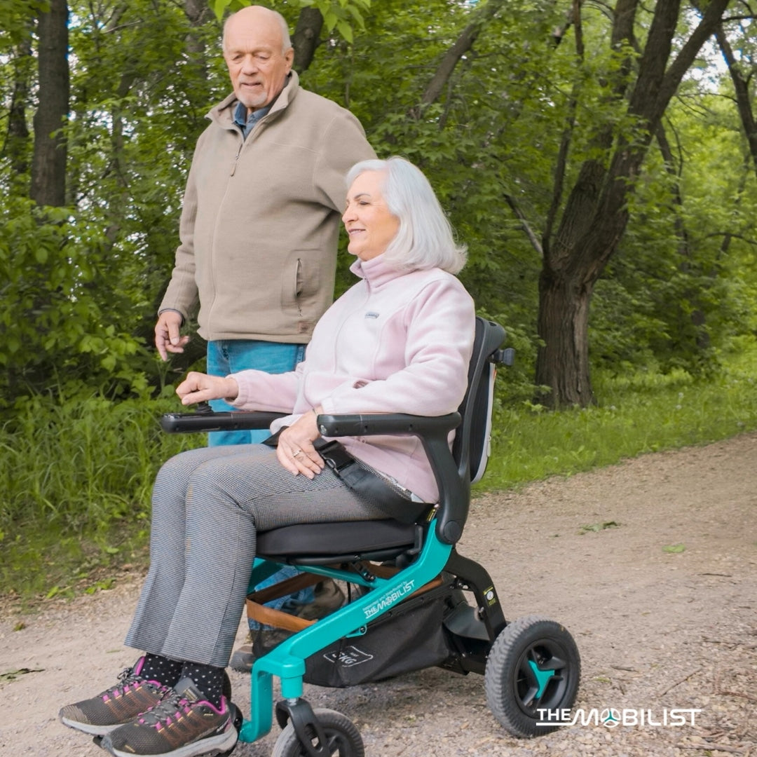 Lifestyle shot of an older couple outdoors on a paved park path, with the man comfortably riding the modern Robooter E40 electric wheelchair.