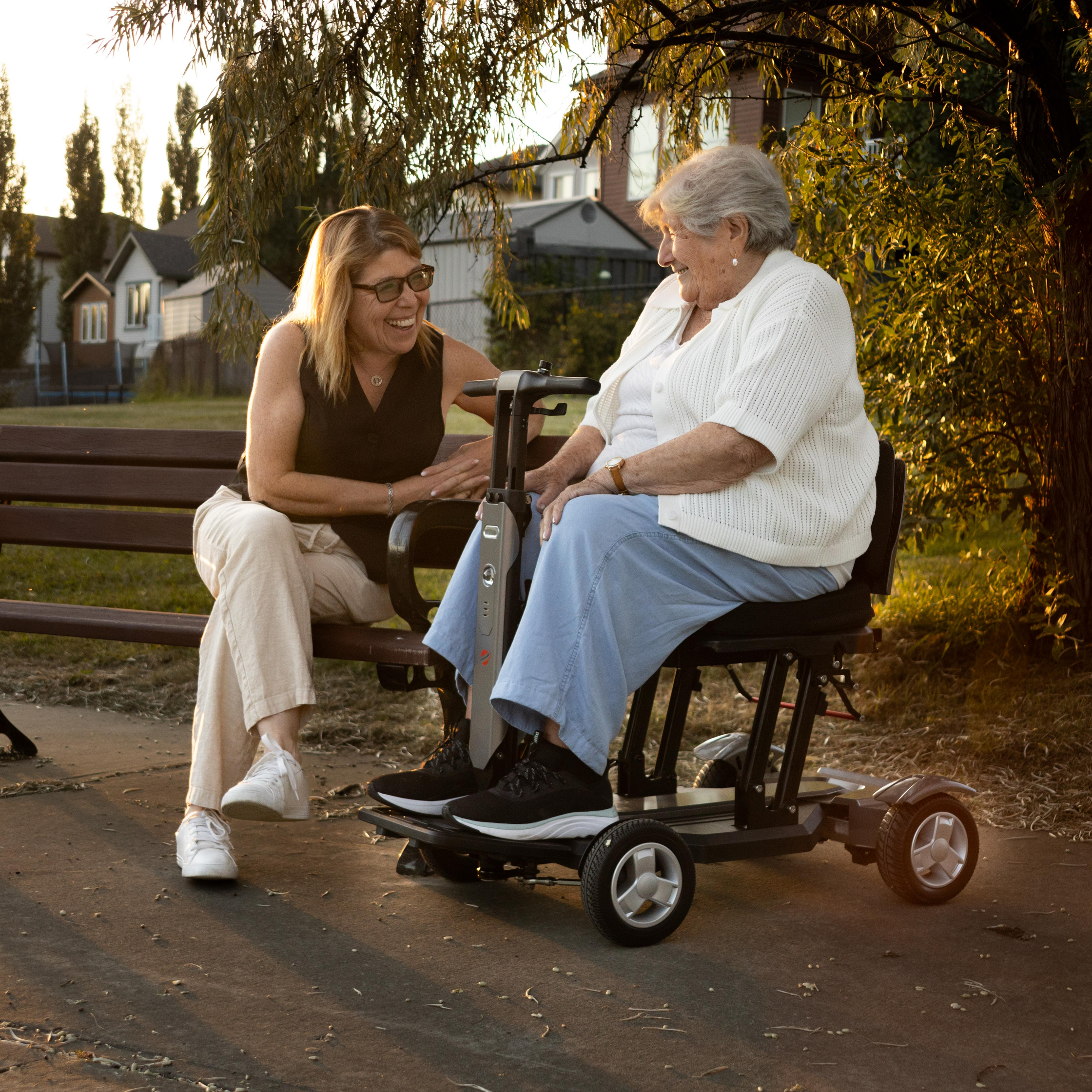 Two women beside a Travel Buggy HELIX scooter outdoors