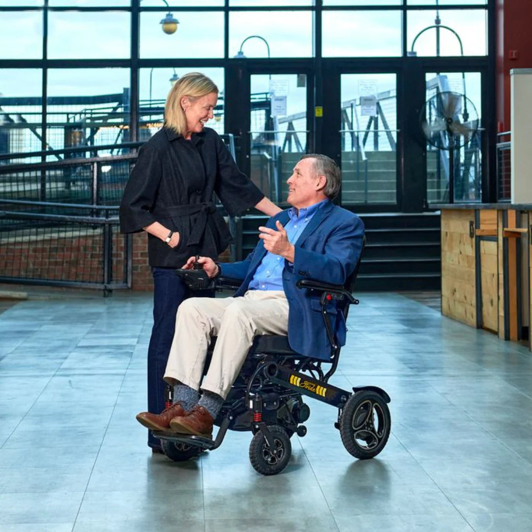 Lifestyle shot of an older couple enjoying an indoor walk, with the woman comfortably driving the Golden Stride GP301 power chair.