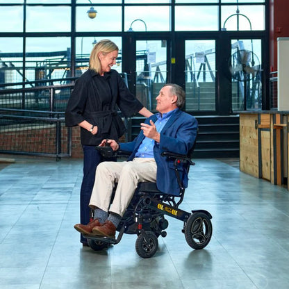 Lifestyle shot of an older couple enjoying an indoor walk, with the woman comfortably driving the Golden Stride GP301 power chair.