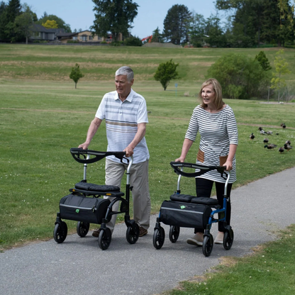 A couple enjoying a sunny outdoor walk together, with the woman comfortably utilizing the pink Evolution Trillium rollator.