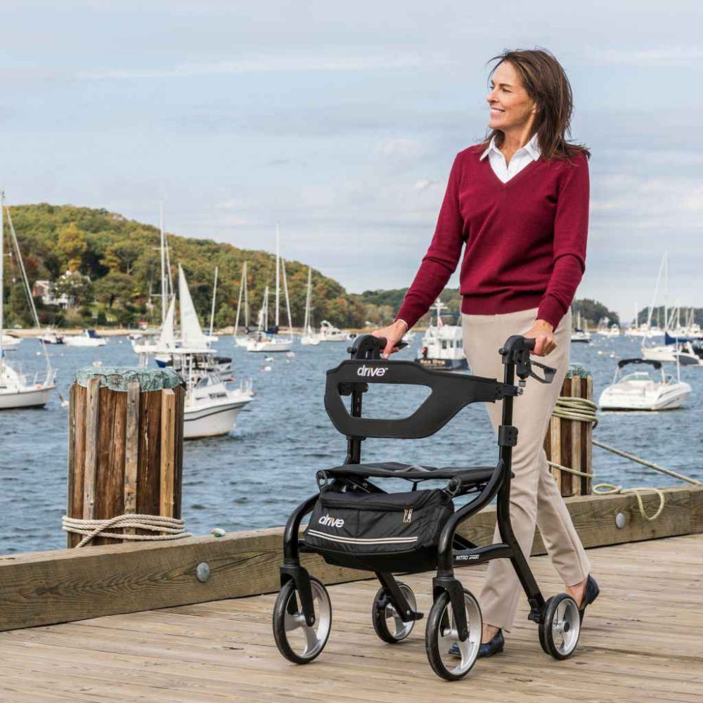 Woman standing with a Black Drive Medical Nitro Sprint rollator beside a marina