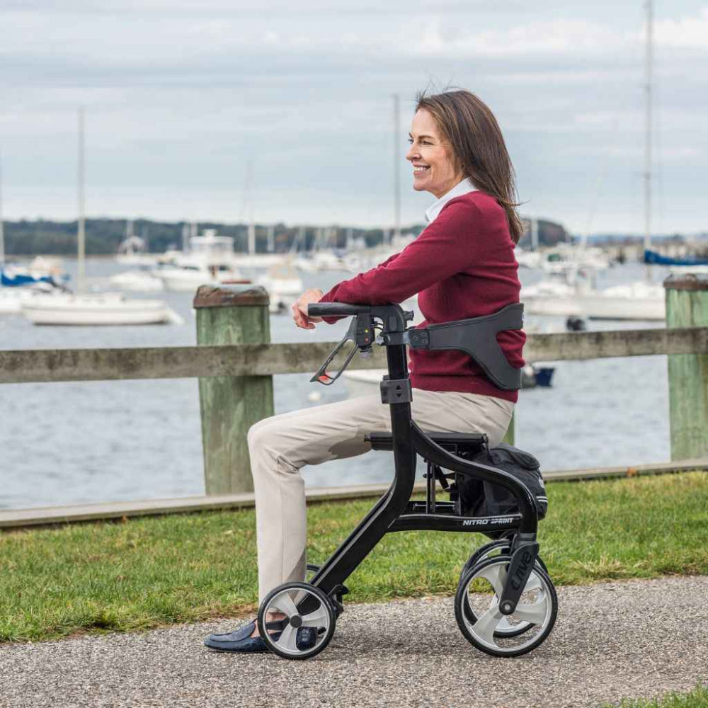 Woman seated on a Black Drive Medical Nitro Sprint rollator beside a marina