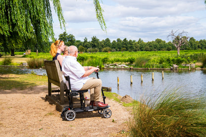 Rider seated on the eFOLDi Compass beside a park pond, shown with optional armrests