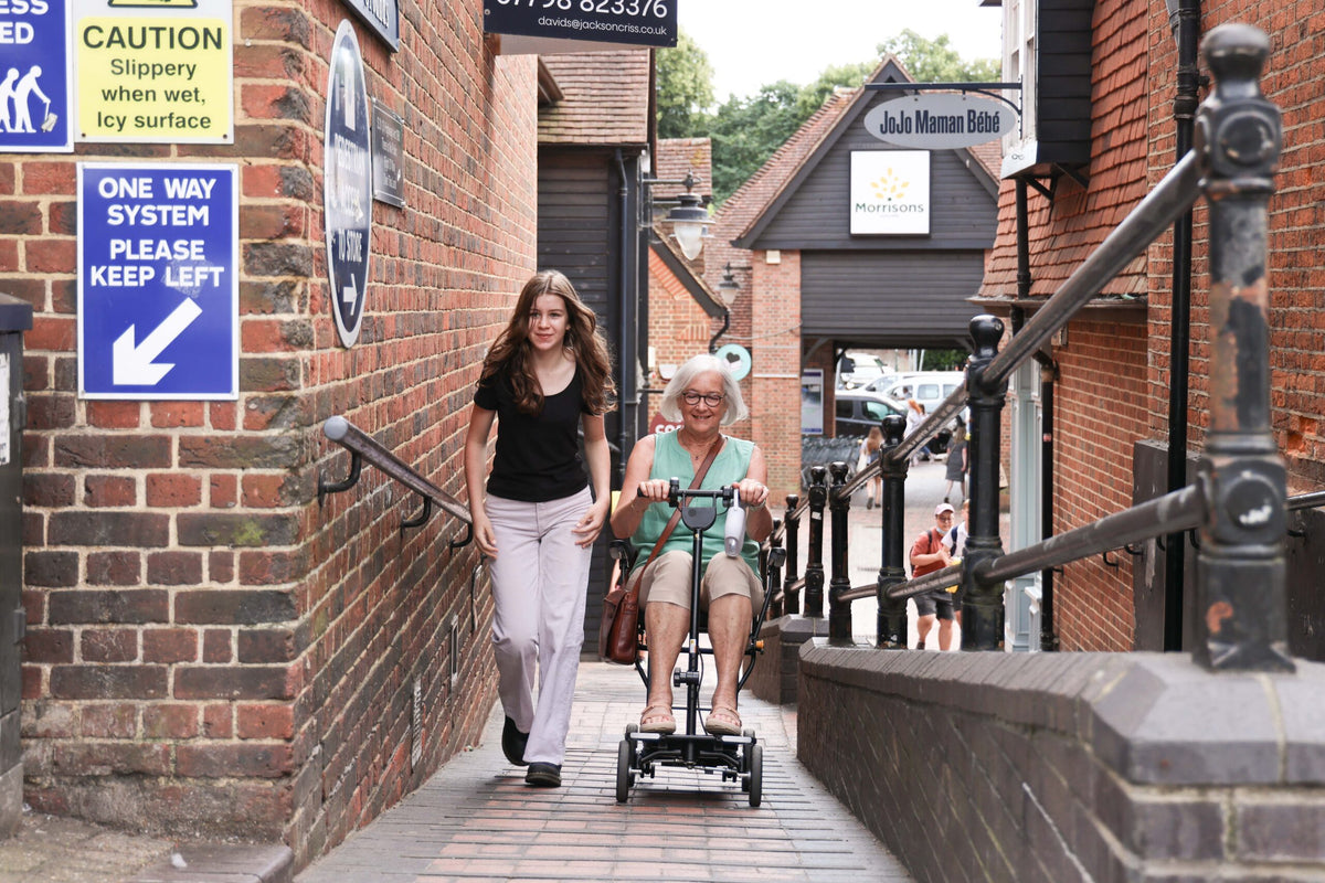 eFOLDi Compass travelling along a town pathway with a companion, shown with optional armrests