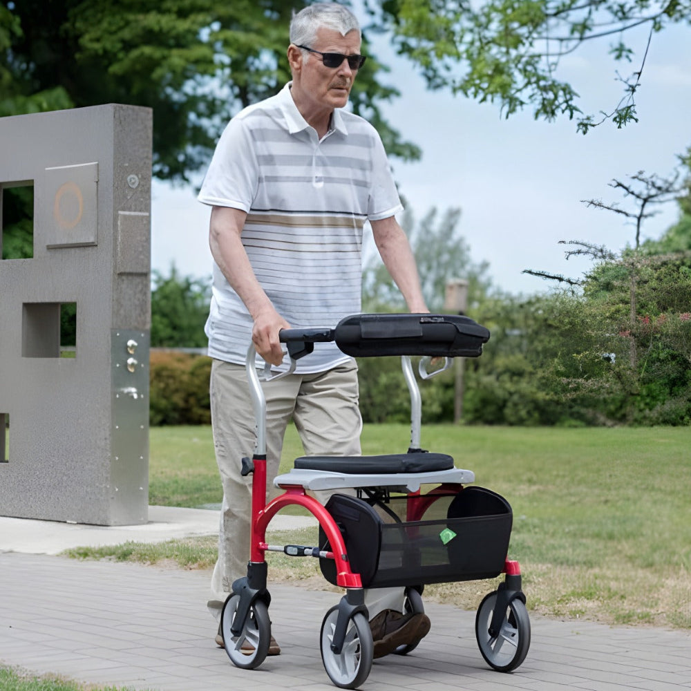 Senior man walking outdoors using the red Evolution Xpresso Lite CF rollator for mobility support.