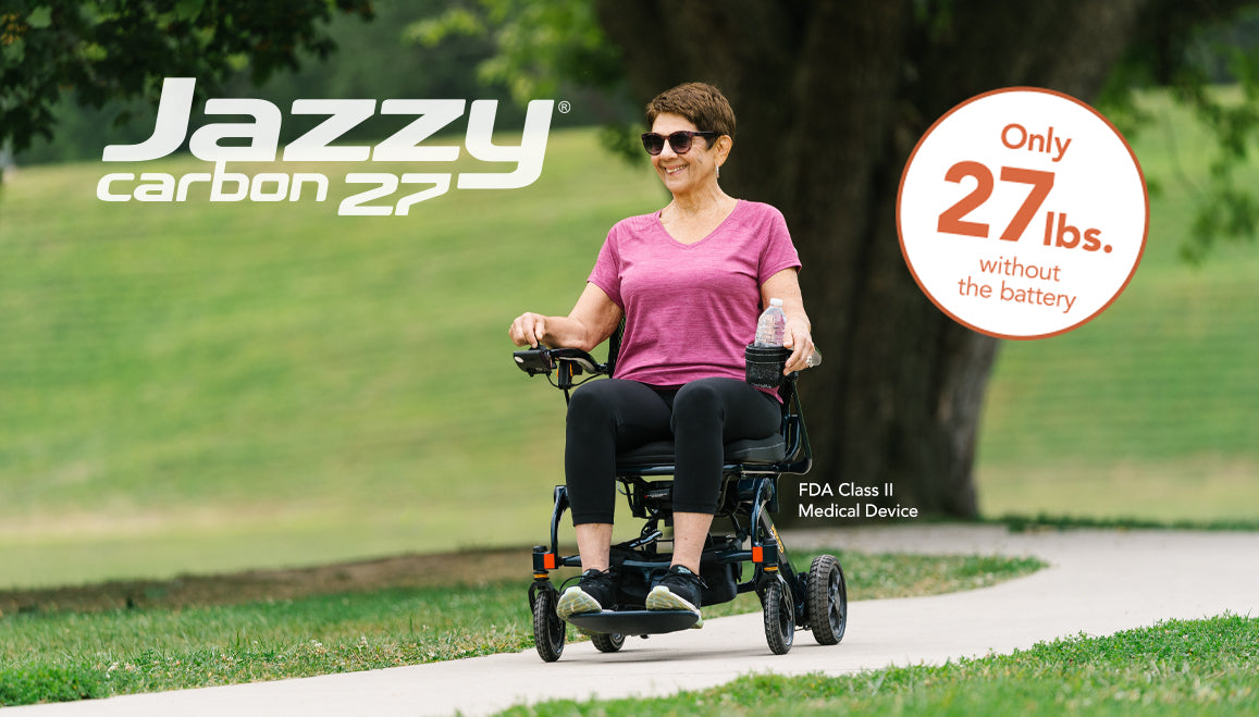 Woman using a Pride Jazzy Carbon 27 power wheelchair on a paved path beside grass