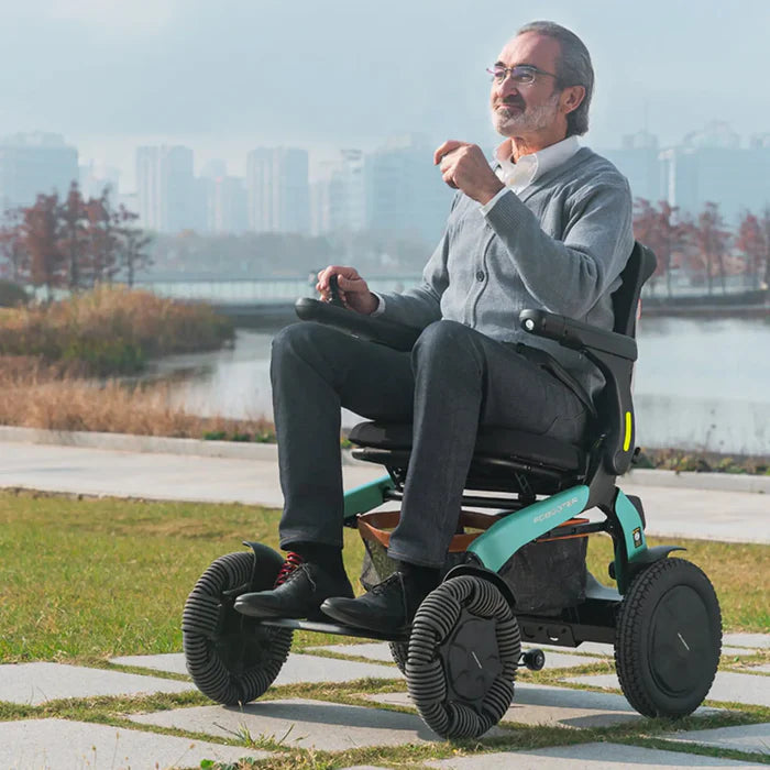 Lifestyle image of a man confidently driving the turquoise Robooter E60 electric wheelchair along a paved path near the water.