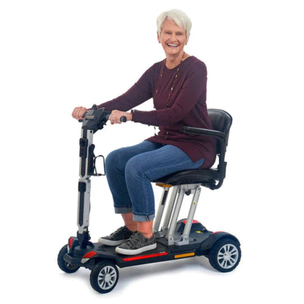 Lifestyle shot of a senior man comfortably riding the Buzzaround CarryOn travel scooter indoors.