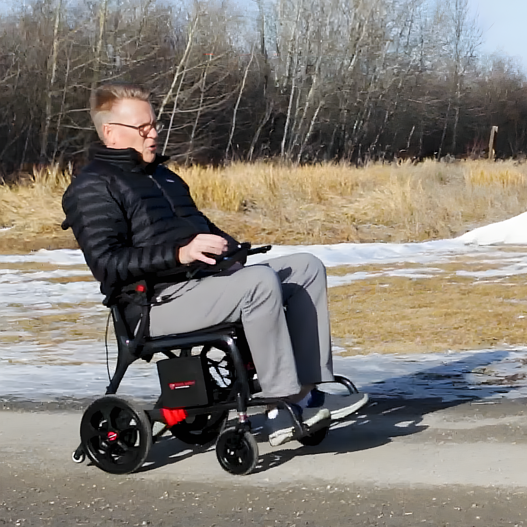 Lifestyle shot of a man comfortably riding the Travel Buggy AEROLUX power chair through a sunny park setting.