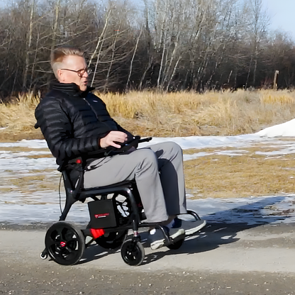 Lifestyle shot of a man comfortably riding the Travel Buggy AEROLUX power chair through a sunny park setting.