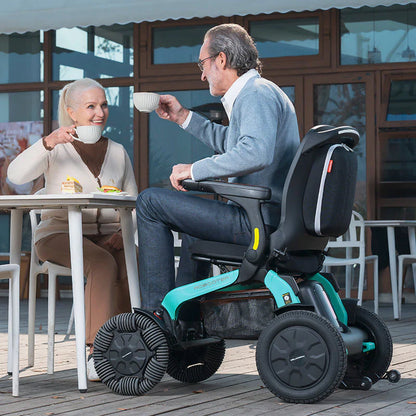 Lifestyle shot of two men chatting outdoors by a scenic railing, with one comfortably seated in the turquoise Robooter E60 power chair.