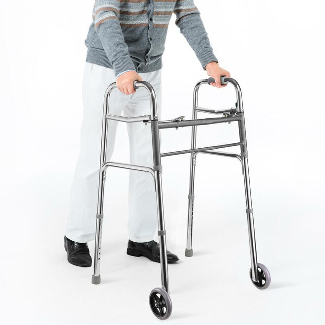 Lifestyle shot of a person safely navigating an indoor home hallway near a staircase using the Care Made folding walker with wheels.