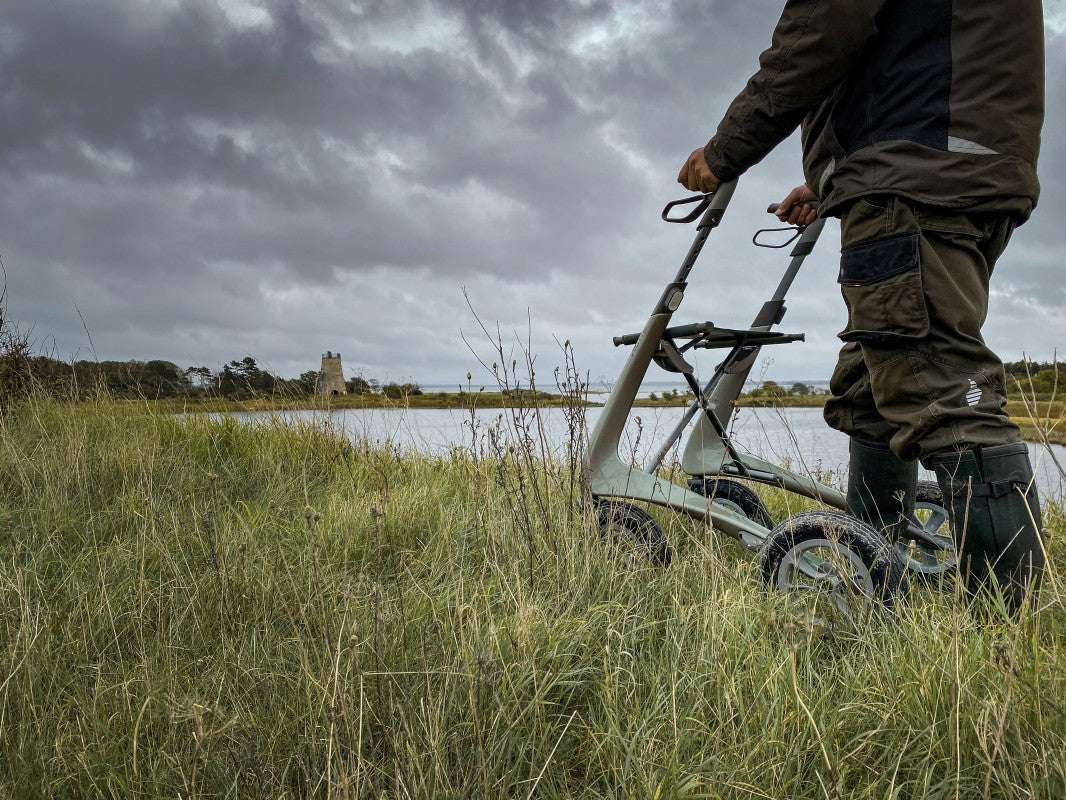 Lifestyle shot of a person confidently navigating through tall outdoor grass using the byACRE Carbon Overland all-terrain rollator.
