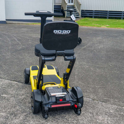 Rear angled view of the Pride Mobility Go Go Carbon folding scooter in yellow, featuring a comfortable seat and sturdy wheelbase.