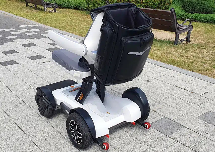 Lifestyle shot of the sleek Robooter X40 backpack securely mounted to the rear of a white X40 electric wheelchair outdoors.