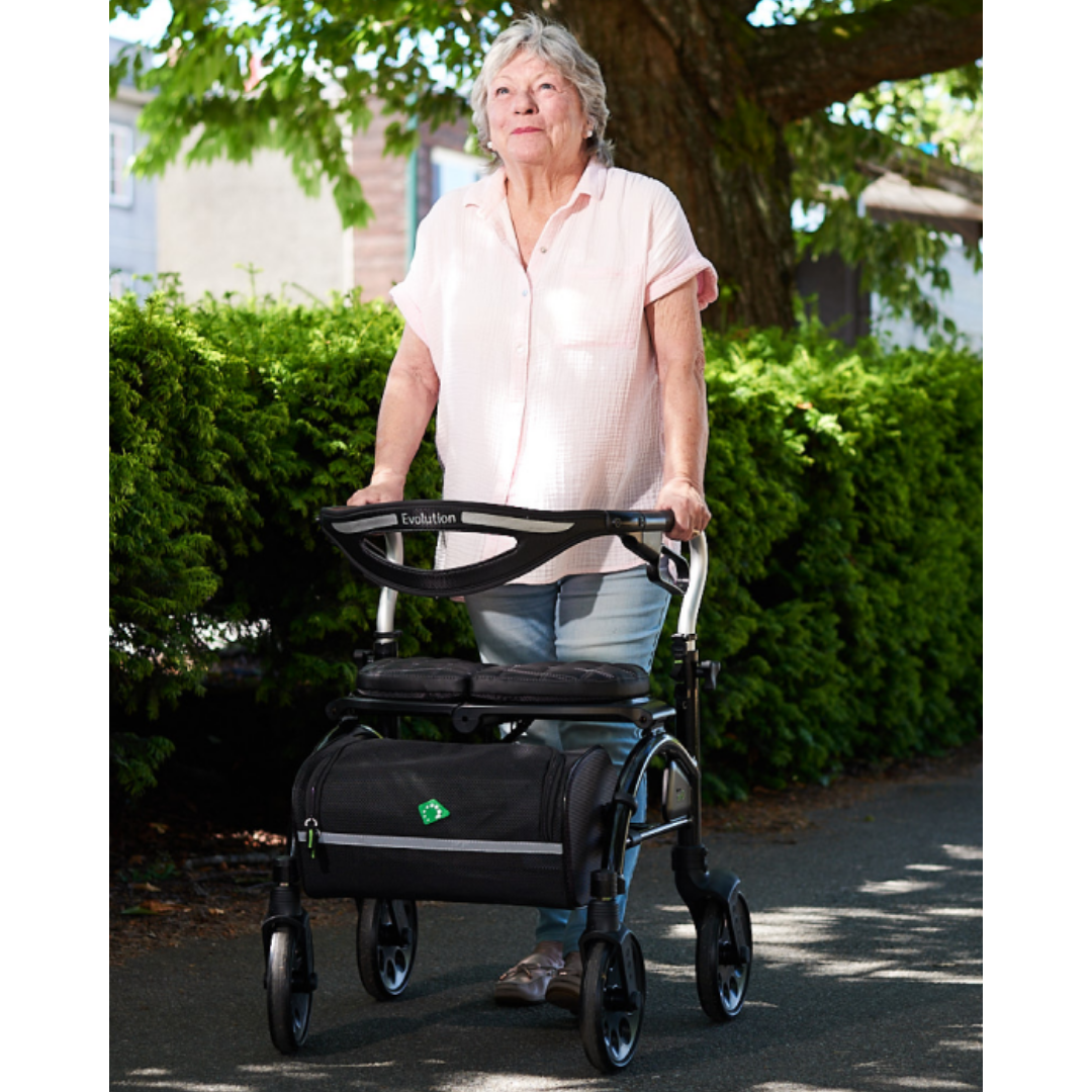 Lifestyle shot of a senior man confidently walking outdoors on a paved path using the black Evolution Trillium rollator for support.