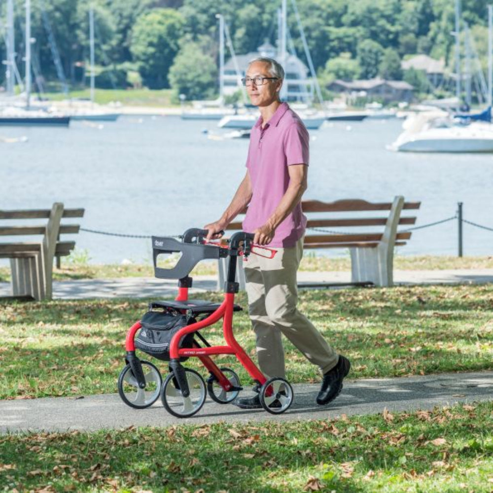 Lifestyle shot of a senior man safely walking along an outdoor paved path using the red Drive Medical Nitro Sprint Rollator.