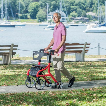 Lifestyle shot of a senior man safely walking along an outdoor paved path using the red Drive Medical Nitro Sprint Rollator.